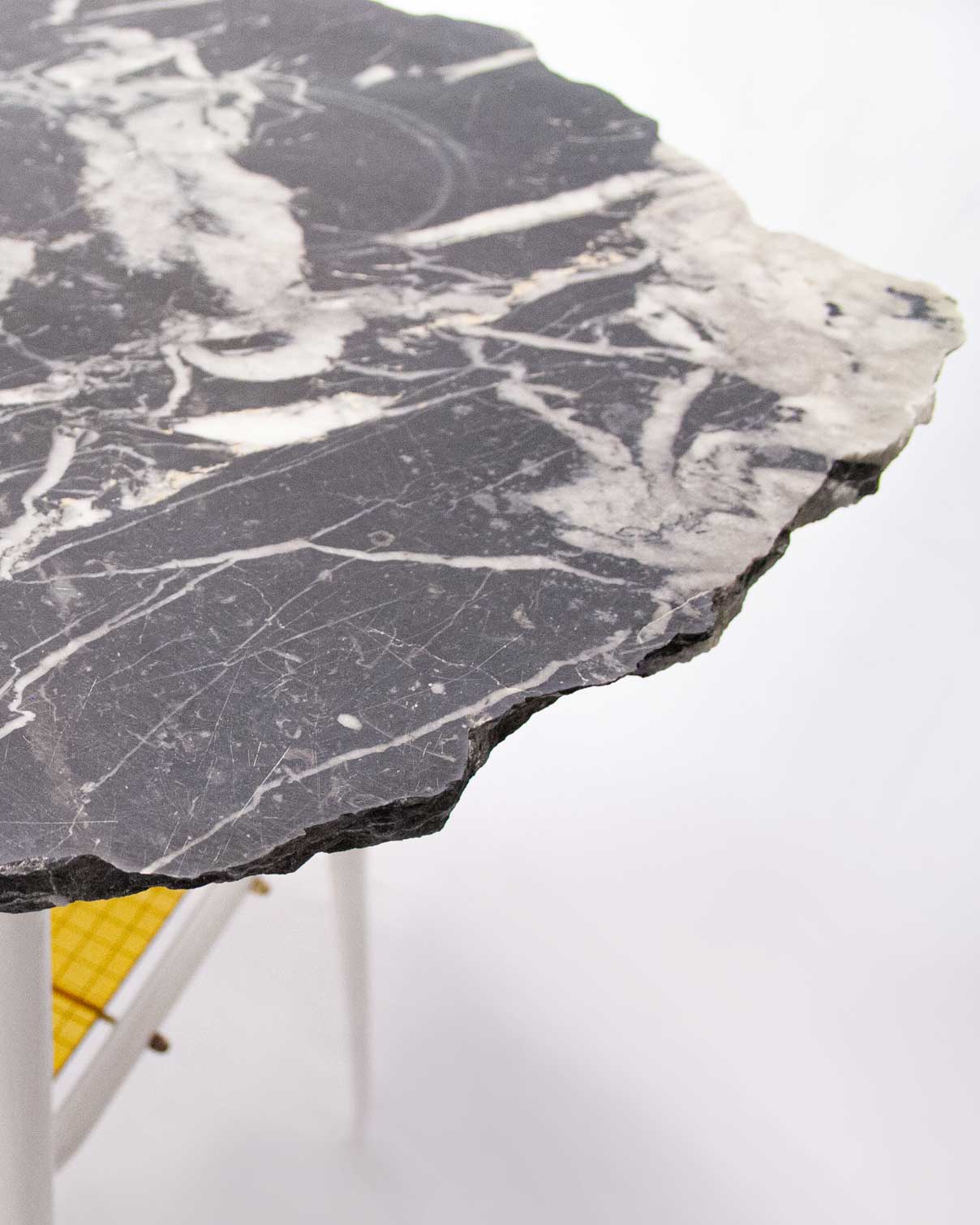 "The 'Lithic Side Table,' created by Jannis Schäfer Studio, is made from reclaimed black marble (nero Marquina) and wired glass, set on an unwanted table frame. This upcycled, recycled, and transformed piece is part of a series of derivative designs. The table features a black marble top with white veining and a yellow wired glass shelf beneath."
