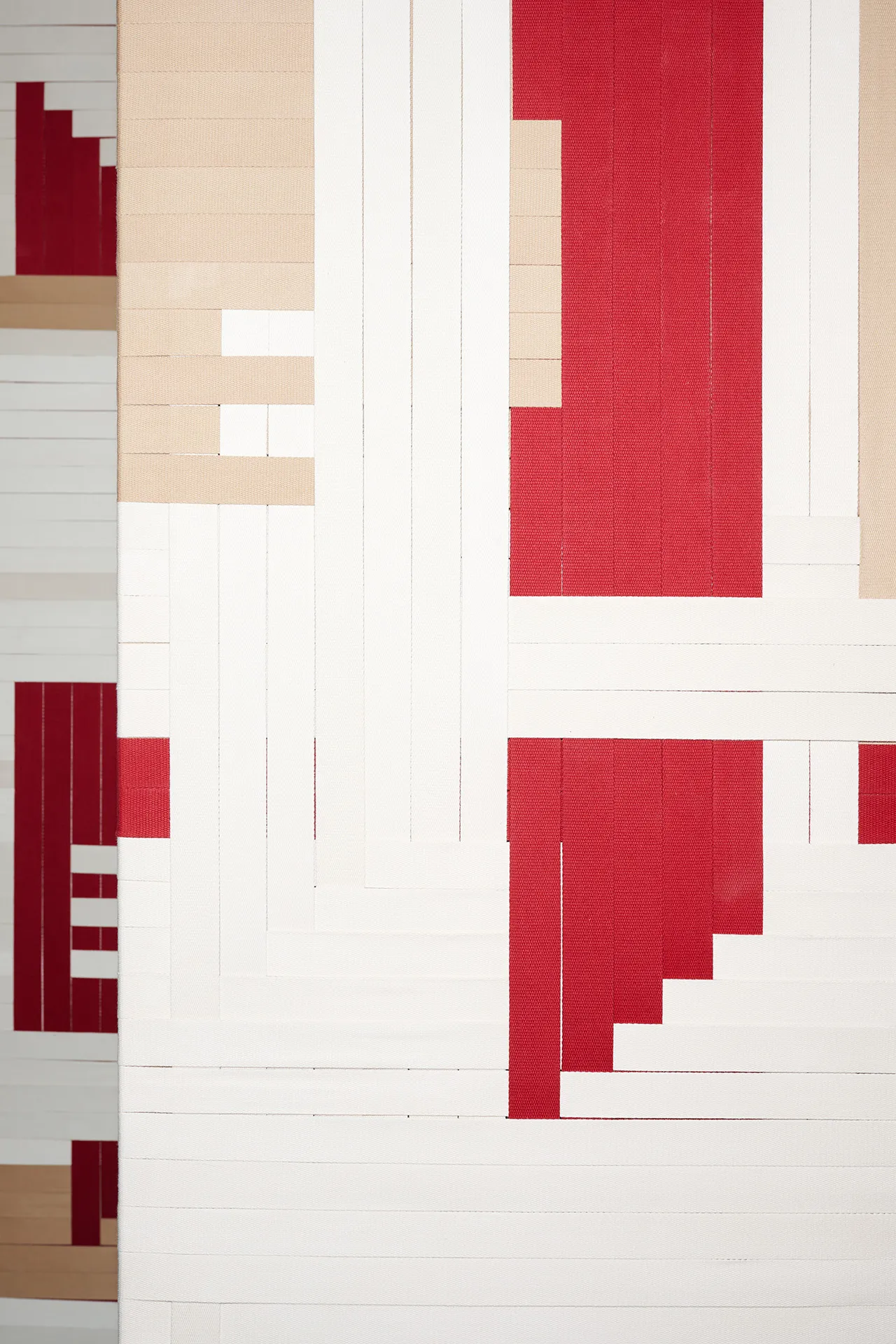 The 'Spinning Jenny,' a project created by Jannis Schäfer Studio in collaboration with INpuls interior studio for Acterience. The image shows a modern office space with sound panels featuring woven graphics made from colored cotton bands in red, white, and beige. The panels are suspended from the ceiling and can spin, adding a dynamic and artistic element to the space.